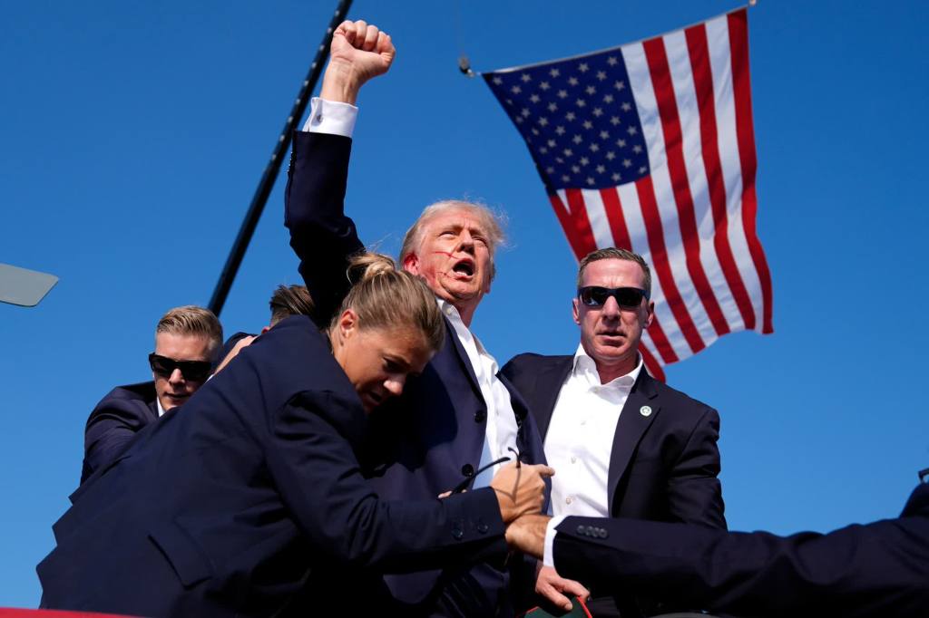 Former President Donald Trump, with blood on his face, raises his fist to the crowd as he is surrounded by Secret Service agents at his campaign rally in Butler,  (Evan Vucci/AP)